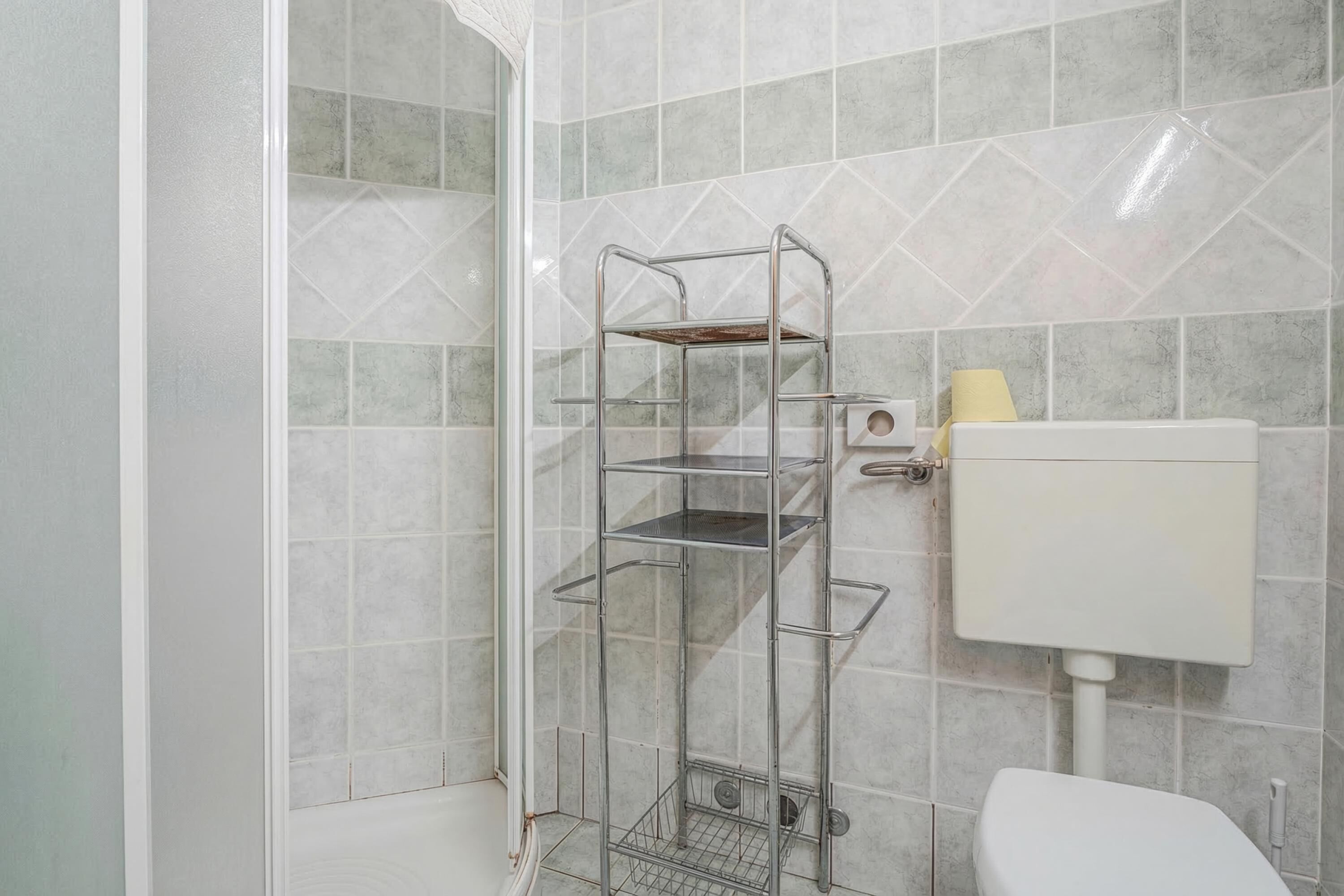 Un bagno con un mobiletto portante in metallo, un water e una parete rivestita di piastrelle.