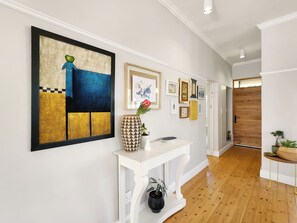 Een gang met een witte console tafel, een groot abstract schilderij en diverse ingelijste foto’s aan de muur.
