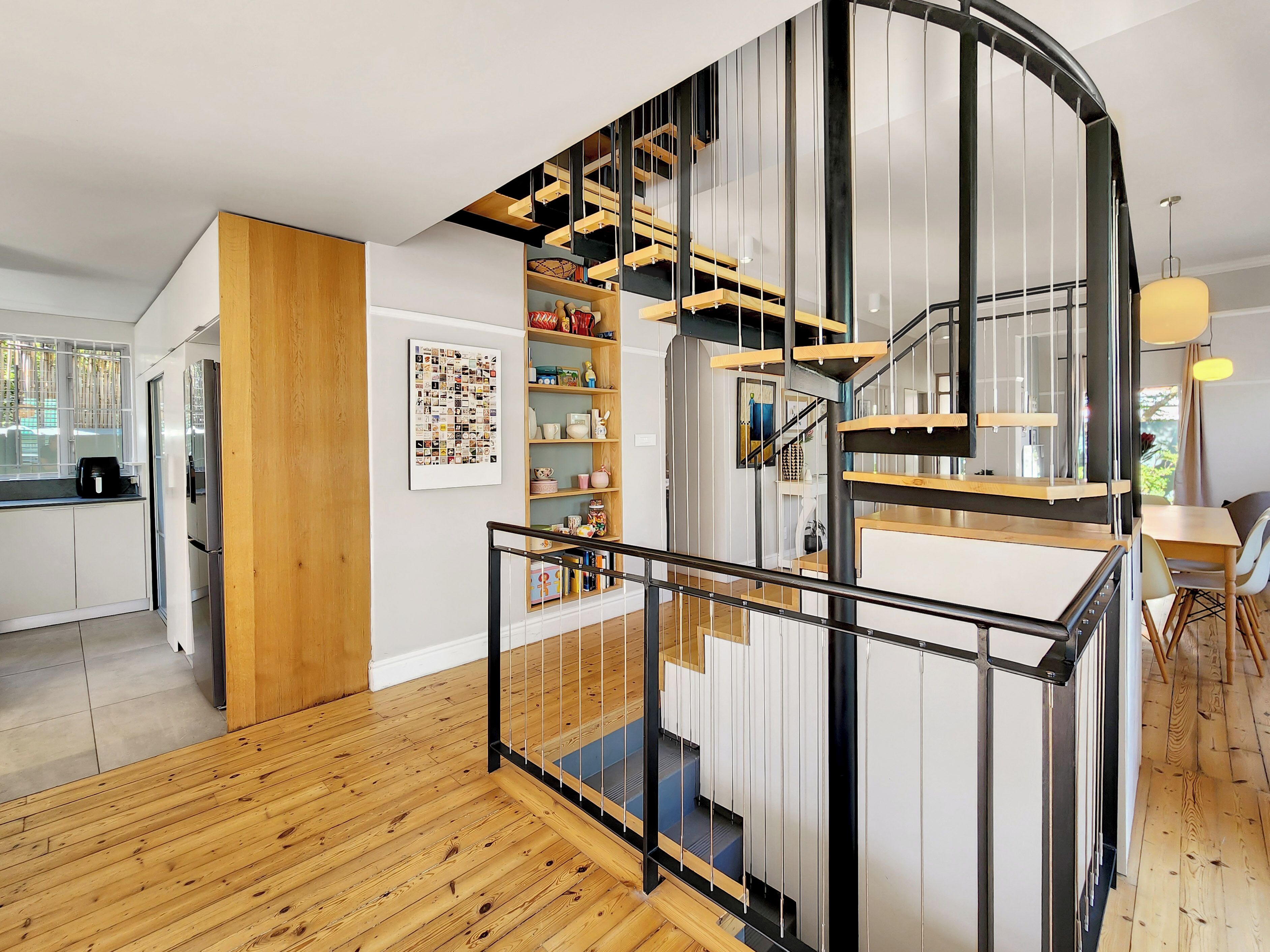 A modern kitchen with white cabinets, a wooden floor, and a spiral staircase with black railings.
