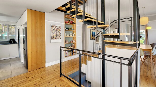 Une cuisine moderne avec des meubles blancs, un plancher en bois et un escalier en colimaçon doté de rampes noires.