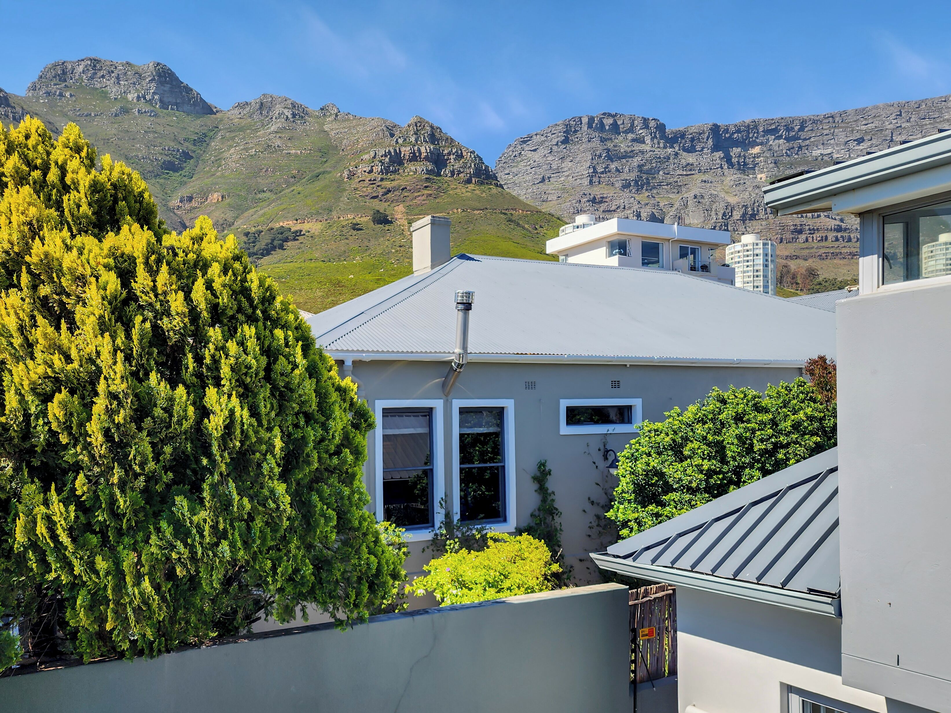 Une maison moderne avec un toit gris, entourée d’une végétation luxuriante et avec des montagnes en arrière-plan.