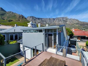Een modern huis met een glazen conservatorium, een houten terras en uitzicht op de bergen.