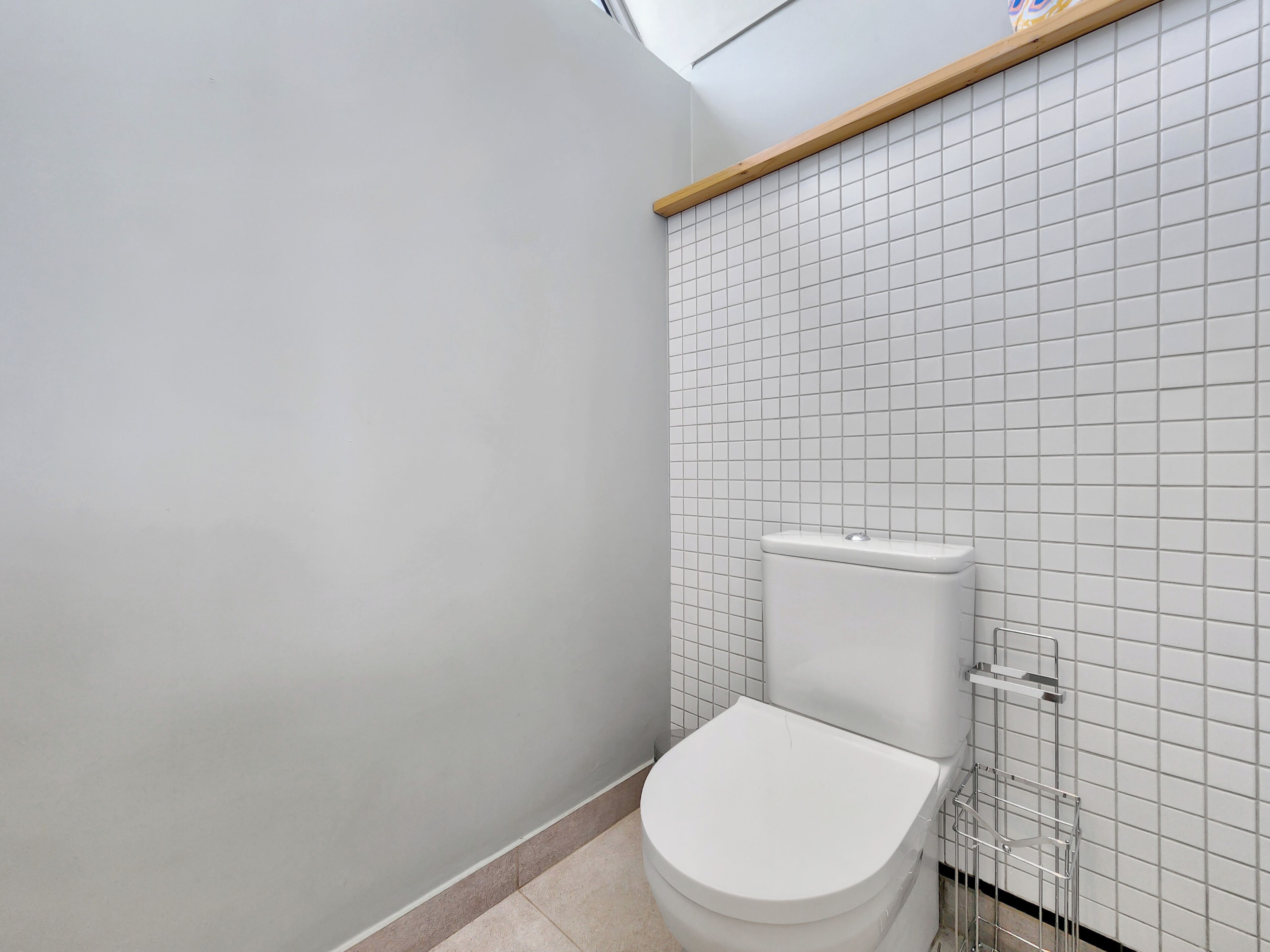 Ein Badezimmer mit weißer Toilette, gefliesten Wänden und einem Holzregal darüber.