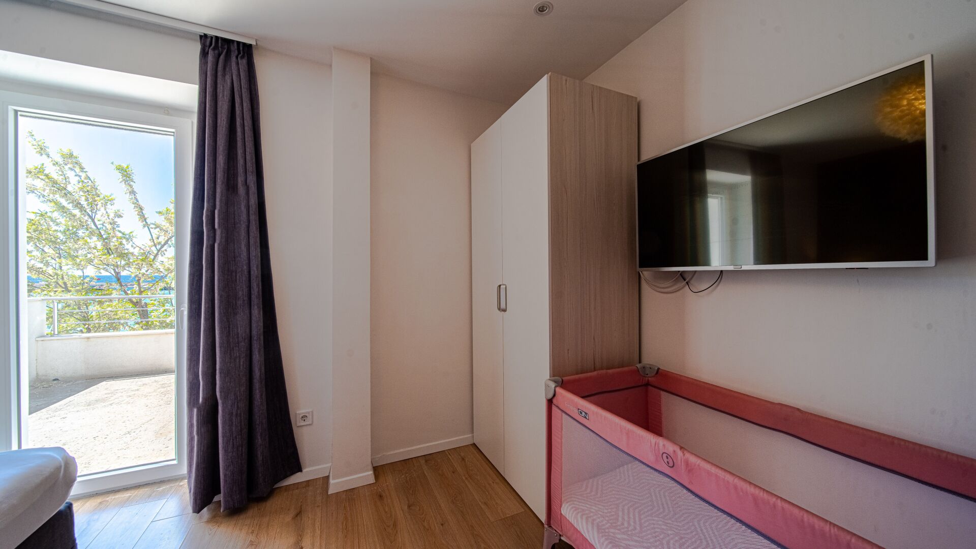 A room with a sliding glass door, a TV mounted on the wall, and a red bed.