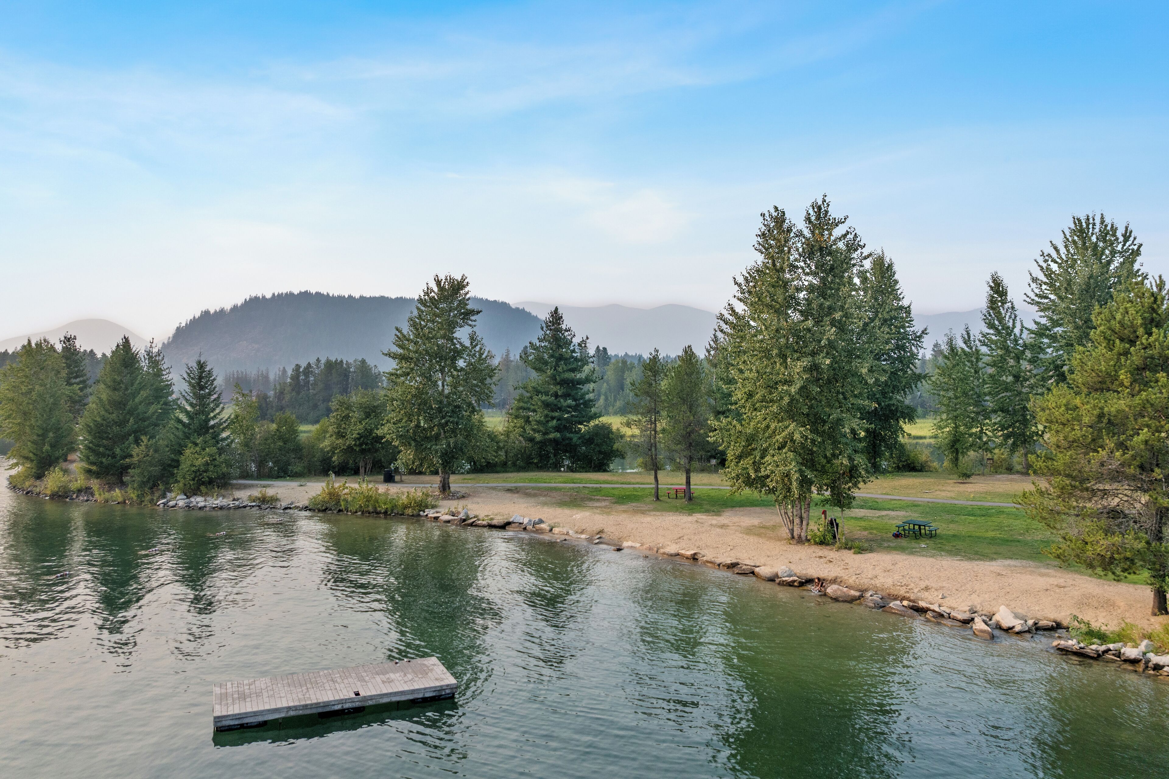 A tranquil lakeside setting with a dock, trees, and a distant mountain range.