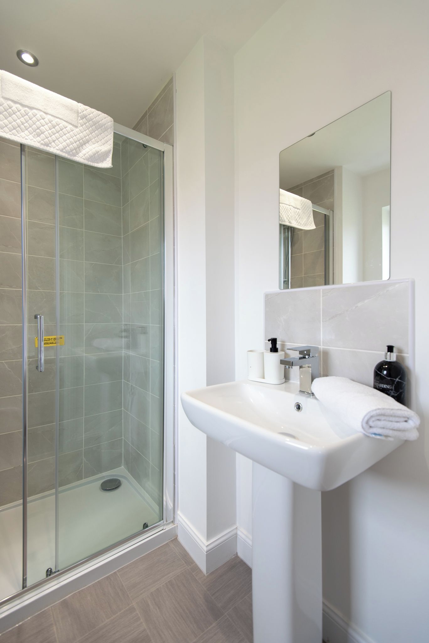 A modern bathroom with a glass-enclosed shower, a white sink, and a large mirror.