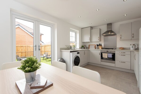 A modern kitchen with white cabinets, a stainless steel range hood, and a built-in oven.