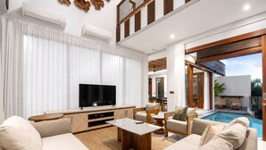 A modern living room with a flat-screen TV, a pool, and a dining area. - 5-BR Beach Villa in Canggu Overlooking Rice Fields (Kuta Utara)