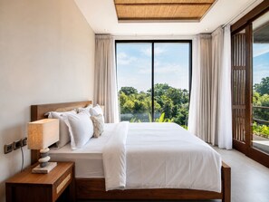 A bedroom with a large bed, a bedside lamp, and a view of greenery through a window. - 5-BR Beach Villa in Canggu Overlooking Rice Fields (Kuta Utara)