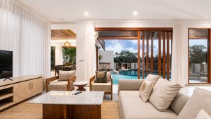 A modern living room with a pool view, a TV, and a dining area. - 5-BR Beach Villa in Canggu Overlooking Rice Fields (Kuta Utara)