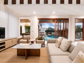 A modern living room with a pool view, a TV, and a dining area.