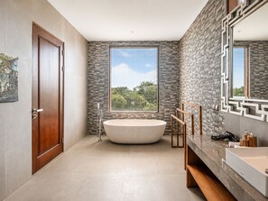 A modern bathroom with a freestanding bathtub, a large mirror, and a stone accent wall.