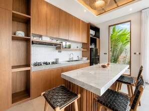 A modern kitchen with wooden cabinets, a marble countertop, and a dining area with black leather chairs.