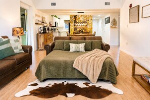 A bedroom with a large bed, a cowhide rug, a brown leather sofa, and a dining area with a chandelier.