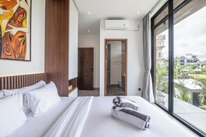 Una camera d'albergo con un letto grande, un quadro appeso al muro, un condizionatore d'aria e vista sulla città da ampie finestre.