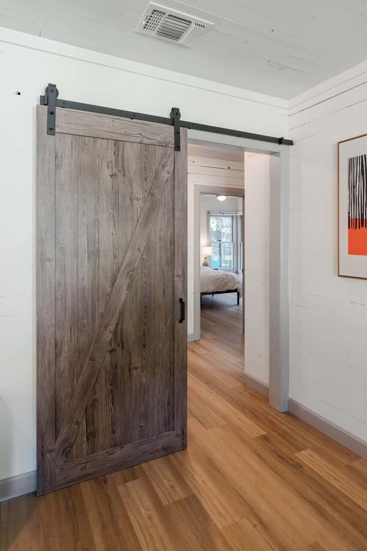 Una habitación con piso de madera, una puerta corrediza de estilo rústico y una cama al fondo.