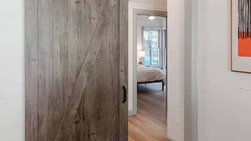 Una habitación con piso de madera, una puerta corrediza de estilo rústico y una cama al fondo.