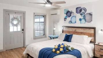 A bedroom with a bed, a ceiling fan, a nightstand, a lamp, and a wall with abstract art.