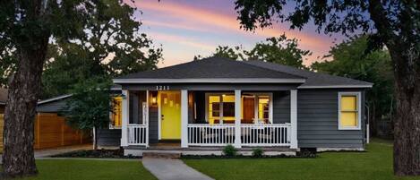 A two-story house with a front porch, numbered 1211, surrounded by trees and a well-maintained lawn.
