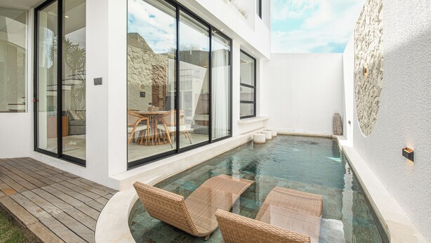A modern pool area with glass walls, wicker lounge chairs, and a stone wall. - Modern 2BR Villas • Stylish Stay in Central Canggu (Canggu)
