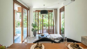 A dining area with a view of a pool and garden, featuring a wooden table, chairs, and a hanging light fixture. - Elegant 1BR Retreat • Jungle View Hideaway in Ubud (Ubud)