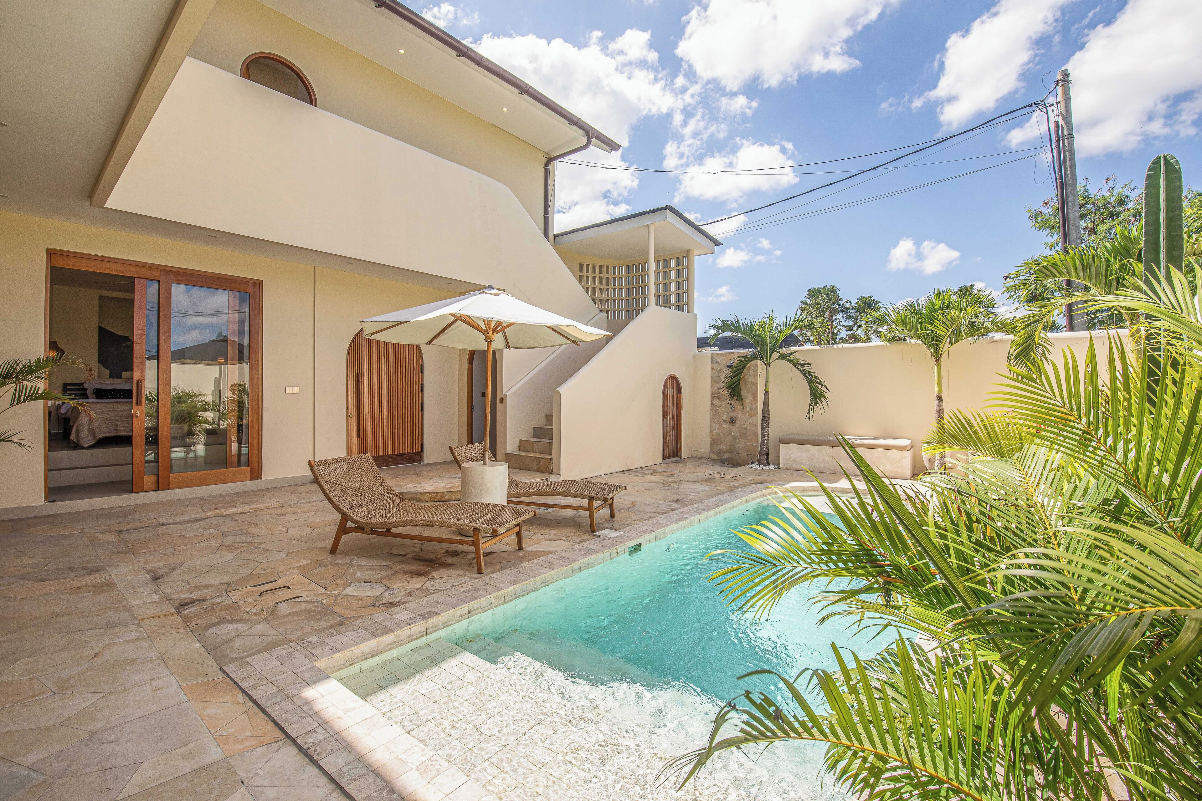 Una casa moderna con piscina, mobiliario exterior y una escalera que lleva a un nivel superior.