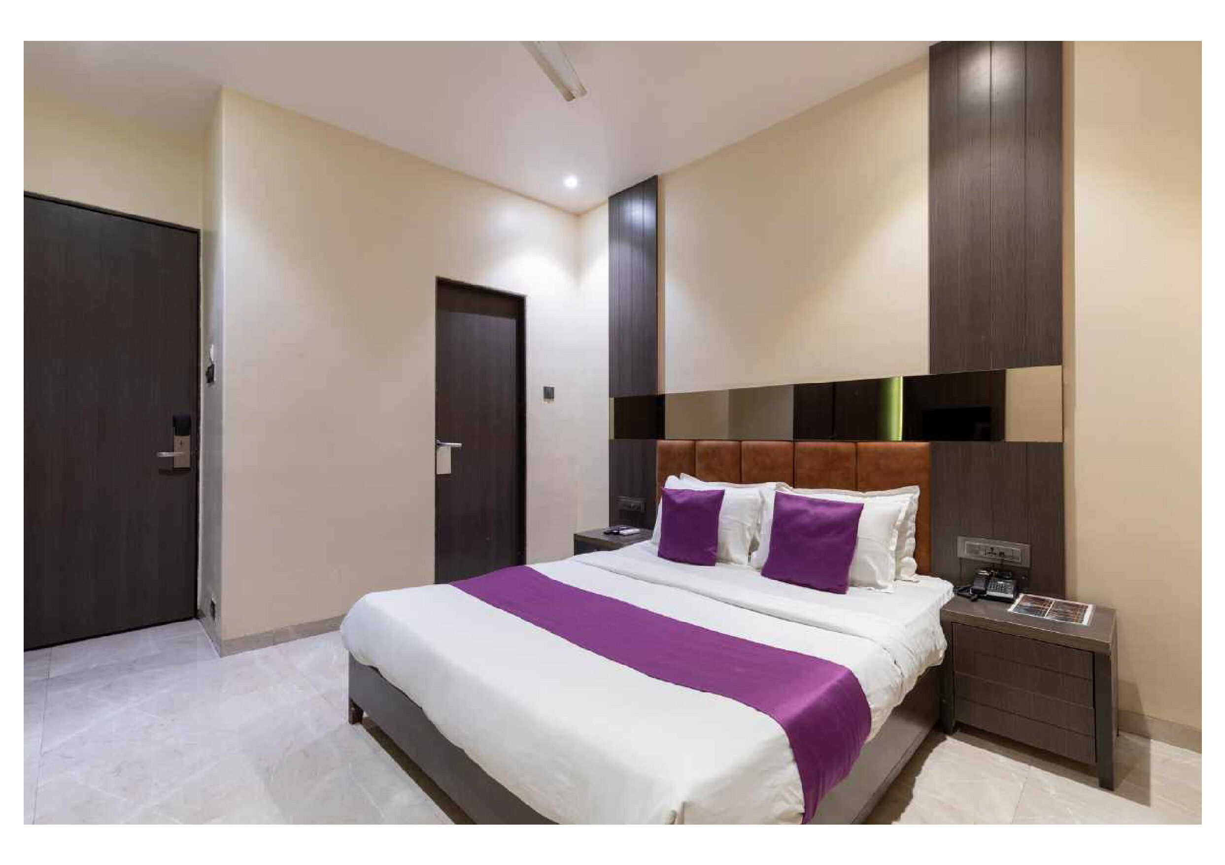Une chambre d’hôtel moderne avec un grand lit, une table de chevet et une tête de lit en bois foncé.