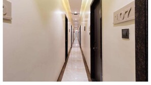 Un pasillo de hotel con suelo de mármol, puertas con números de habitación e iluminación empotrada.