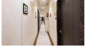 Un pasillo largo y estrecho con paredes blancas y piso de mármol, que conduce a una puerta de madera oscura.
