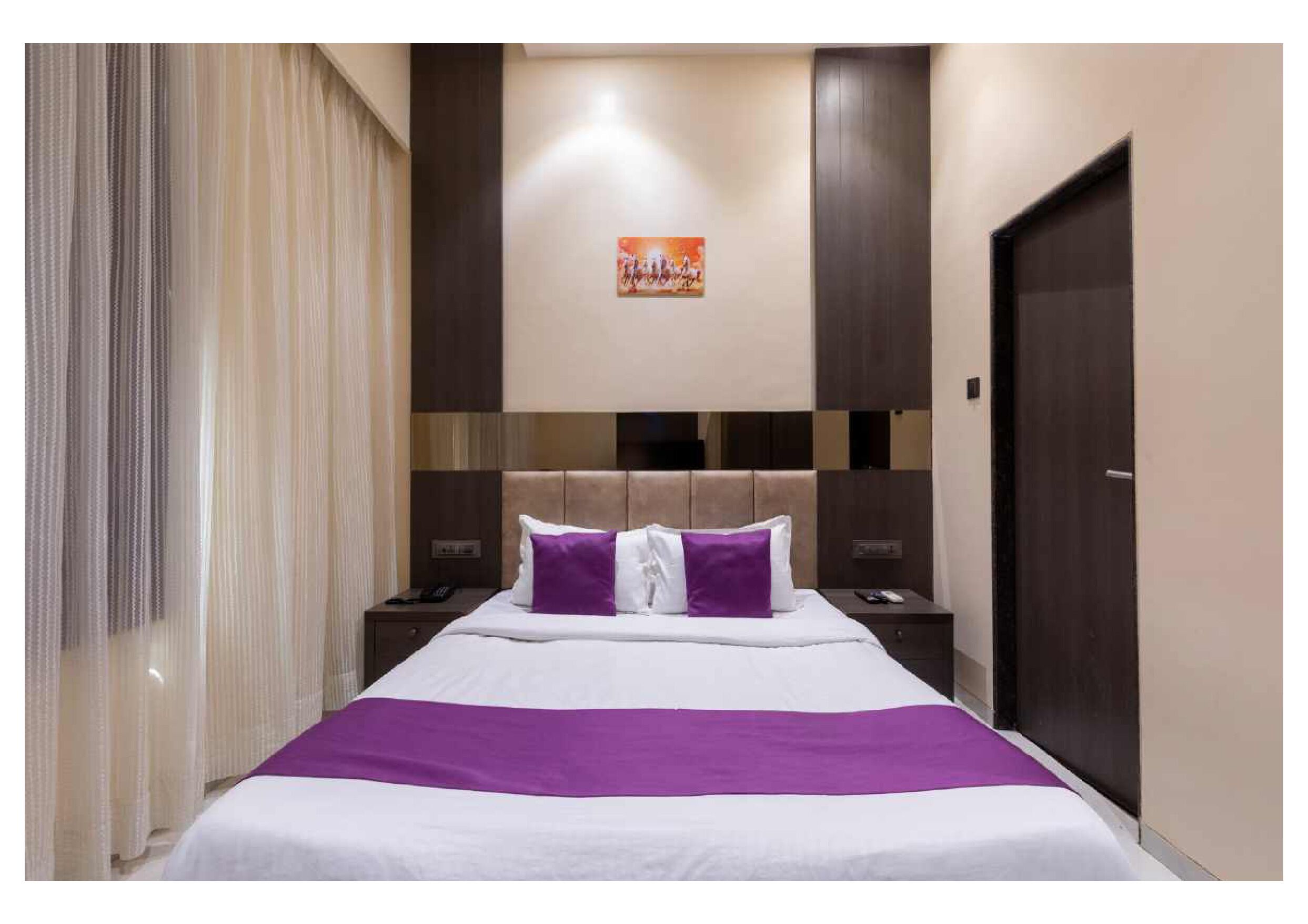 A hotel room with a large bed, two nightstands, a headboard with a decorative panel, a door, and a window with curtains.