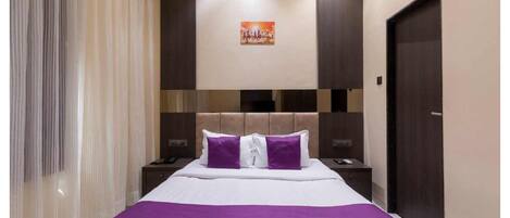 A hotel room with a large bed, two nightstands, a headboard with a decorative panel, a door, and a window with curtains.