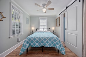 A bedroom with a bed, two bedside lamps, a ceiling fan, and a window with blinds.