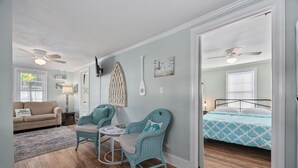 A cozy room with a bed, a sofa, two wicker chairs, a small table, and a ceiling fan.