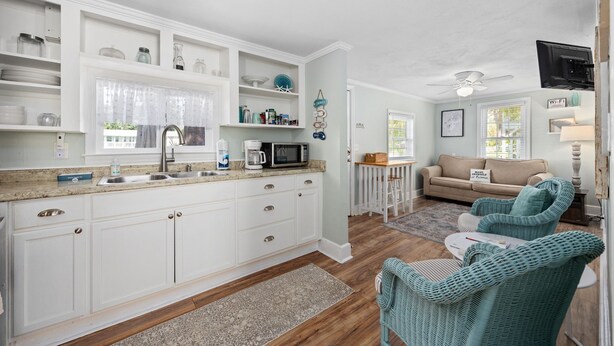 A modern kitchen with white cabinets, a microwave, and a sink. There is a dining area with wicker chairs and a table.