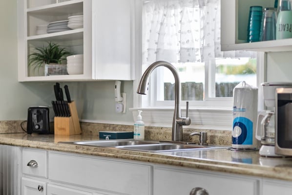 A kitchen with white cabinets, a stainless steel sink, a toaster, and a coffee maker.