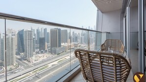 Un balcone con sedie in vimini e un tavolo in vetro, con vista su un paesaggio urbano caratterizzato da edifici moderni e un'autostrada.