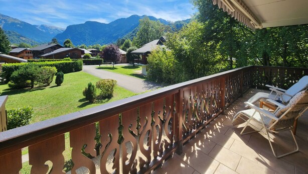 A balcony with a view of a mountainous landscape, a well-maintained lawn, and a wooden fence. - Quiet T3 in Samoëns, near center, WIFI, private parking (Samoëns)
