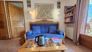 A cozy room with a blue sofa, a wooden coffee table with a kettle, and a bookshelf. - Quiet T3 in Samoëns, near center, WIFI, private parking (Samoëns)