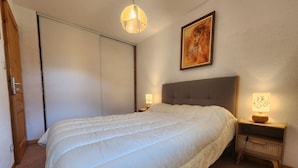 A bedroom with a large bed, a nightstand with a lamp, a ceiling light, a door, and a painting on the wall. - Quiet T3 in Samoëns, near center, WIFI, private parking (Samoëns)