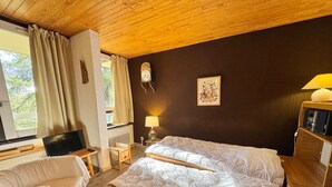 Quarto de hotel com uma cama grande, uma escrivaninha com computador, uma cadeira, uma mesinha e um abajur.