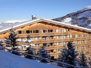 Una cabaña de madera con varios balcones, rodeada de árboles y montañas nevadas.