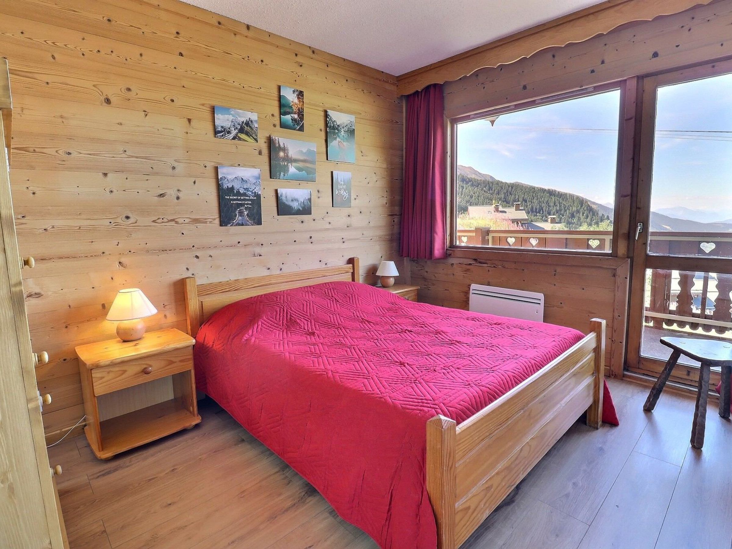 A wooden room with a bed, a nightstand, a lamp, and a window with a view of mountains.