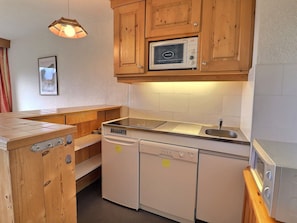 Una cocina compacta con armarios de madera, microondas integrado, lavavajillas y estufa.