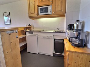 Cocina pequeña con armarios de madera, microondas, cafetera y lavavajillas.