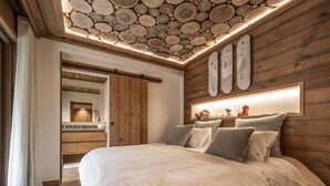 A bedroom with a large bed, wooden walls, a wooden ceiling with a circular pattern, a built-in shelf with decorative items, and a bathroom with a wooden vanity.
