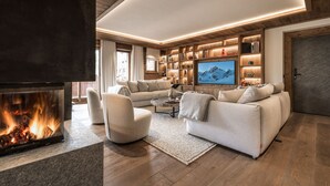 A modern living room with a fireplace, comfortable seating, a television, and wooden shelving with various items.