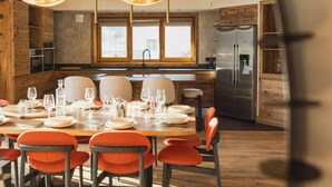Eine moderne Küche mit Holzschränken, einem Edelstahlkühlschrank und einem Essbereich mit orangefarbenen Stühlen und einem Esstisch für sechs Personen.