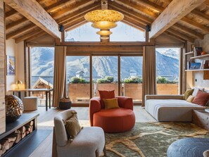 A spacious living room with a large window offering a mountain view, wooden beams on the ceiling, and a cozy seating area with a red chair and a grey sofa. - Exceptional chalet in 3 Valleys, 14 pers, jacuzzi, sauna (Saint-Martin-de-Belleville)