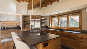 Eine moderne Küche mit einer zentralen Kochinsel, Holzschränken, einem Edelstahlkühlschrank und einem Fenster mit Blick ins Freie.