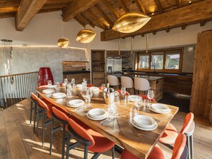 Un espace repas avec une longue table en bois dressée pour le repas, entourée de chaises orange.